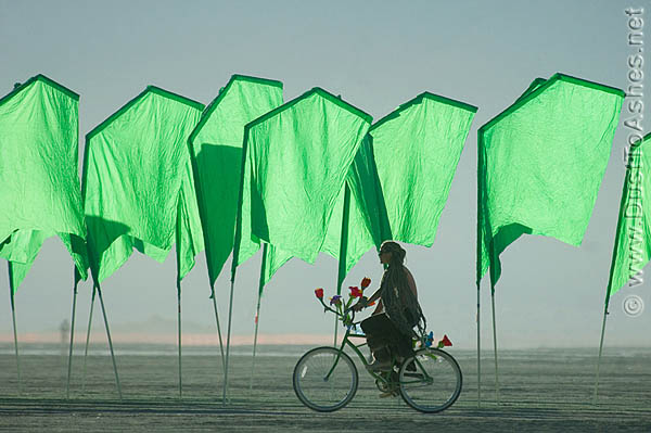 Burning Man girl riding the bicycle in green flag field